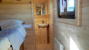 A compact wooden cabin room with a bed, a small sink, and a window.