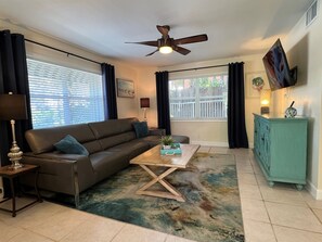 A living room with a sofa, coffee table, TV, and a ceiling fan.
