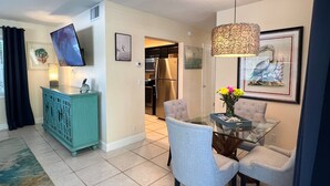 A dining area with a glass table, chairs, a teal cabinet, a hanging light fixture, and a framed picture on the wall. - Ocean Pearl 2 Blocks to A1A-Delray Beach! (Delray Beach)