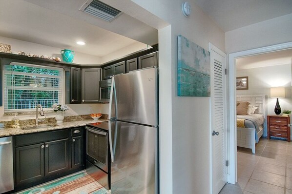 A modern kitchen with dark cabinets, stainless steel appliances, and a window with a view.