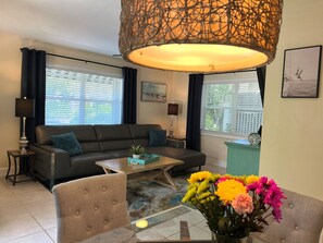 A living room with a sofa, coffee table, armchair, and a vase of flowers.