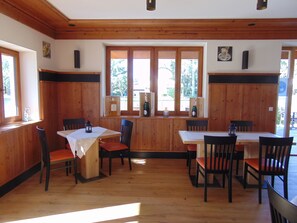 A wooden interior with a dining area featuring tables and chairs, large windows, and wooden paneling. - Hotel Heimfeld Cafe Restaurant (Garching an der Alz)