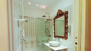 A bathroom with a glass-enclosed shower, a white sink, and a large ornate mirror. - Presidential Suite (Roma)