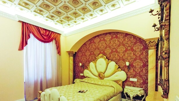 A bedroom with a large bed, ornate headboard, and a decorative ceiling. - Presidential Suite (Roma)
