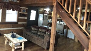A rustic cabin interior with a wooden staircase, a sofa with patterned cushions, a dining table, and a kitchen area. - Foot of the Smokies, quiet wooded paradise. Gatlinburg Pigeon Forge (Cosby)