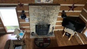 A log cabin interior with a stone fireplace, wooden walls, a mounted television, and a star decoration on the ceiling. - Foot of the Smokies, quiet wooded paradise. Gatlinburg Pigeon Forge (Cosby)