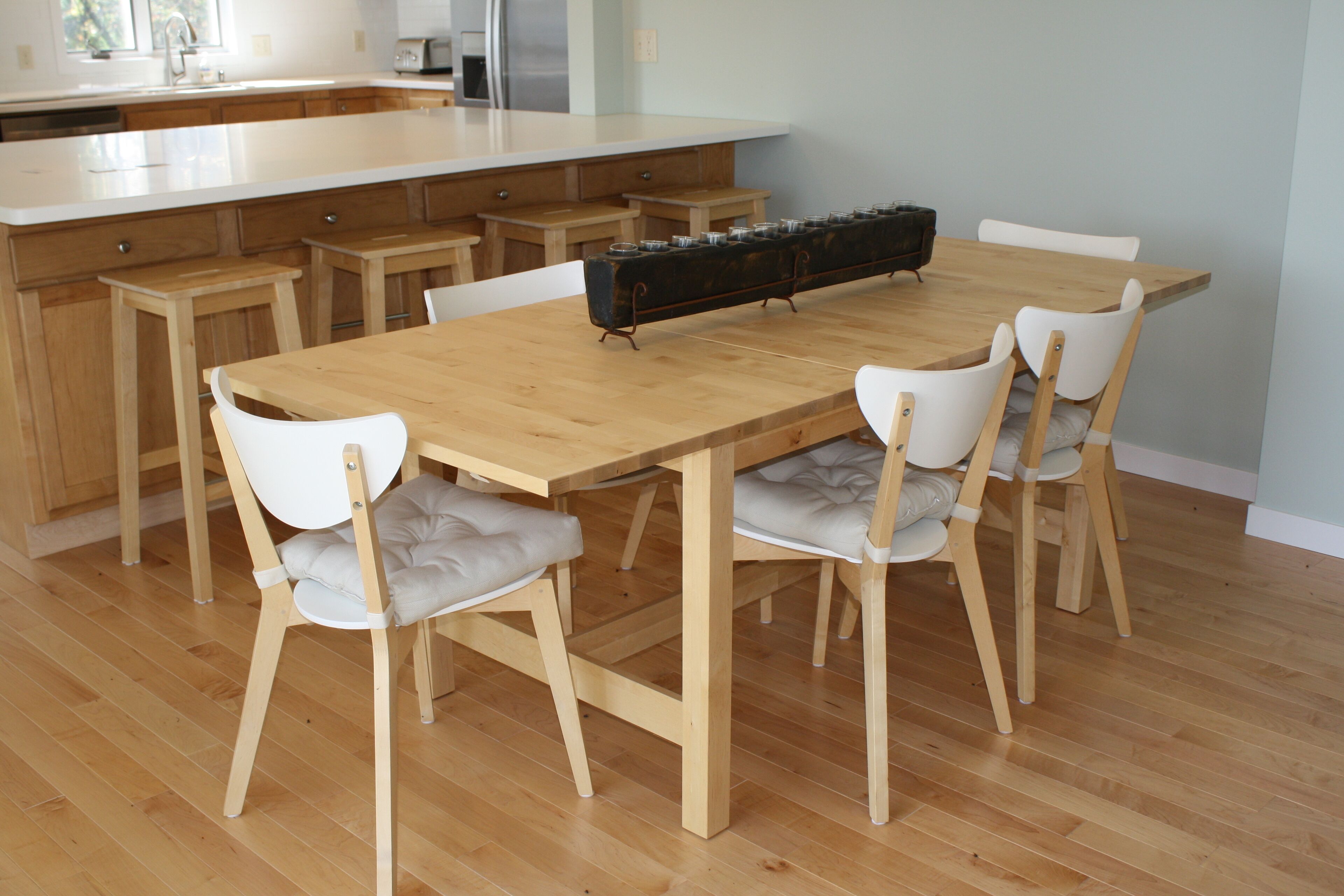 Une cuisine moderne avec une table et des chaises en bois, un îlot central intégré et un long plan de travail agrémenté de bocaux.