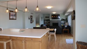 A spacious kitchen with a large island, wooden cabinets, pendant lighting, and a view into the living area.
