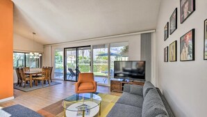 A modern living room with a sofa, coffee table, TV, and dining area with chairs and a table. - Sunrise Villas 3BR condo - Mountain views, relaxing spa & pool and pickleball (Palm Springs)