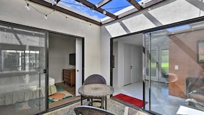 A modern room with a glass door leading to a balcony, a round table, and wicker chairs. - Sunrise Villas 3BR condo - Mountain views, relaxing spa & pool and pickleball (Palm Springs)