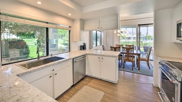 A modern kitchen with white cabinetry, a built-in dishwasher, and a large window overlooking a garden. - Sunrise Villas 3BR condo - Mountain views, relaxing spa & pool and pickleball (Palm Springs)