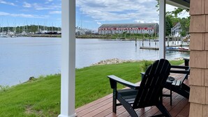 Eine überdachte Terrasse mit zwei Adirondack-Stühlen, Blick auf einen Yachthafen mit Booten und ein Gebäude im Hintergrund mit der Aufschrift "MYSTIC SHIPYARD LLC".