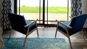 Ein Zimmer mit zwei blauen Stühlen, einem blauen Teppich und Blick auf ein Gewässer durch eine große Schiebetür.