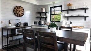 A modern kitchen with a wooden dining table, dark wooden chairs, a large clock, and built-in shelves with kitchenware. - Harbor View Landing Mystic, CT - The Bluffs Waterfront House - First Floor ONLY (Mystic)