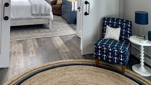A bedroom with a bed, a dresser, a chair, a mirror, and a chandelier. - Harbor View Landing Mystic, CT - The Bluffs Waterfront House - First Floor ONLY (Mystic)