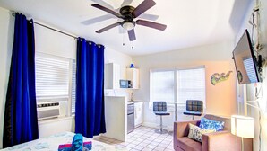 A bedroom with a bed, a ceiling fan, a desk, a chair, a sofa, a TV, and a window with curtains. - Studio 301 Little Paris 1 blk to the beach 1floor (Fort Lauderdale)