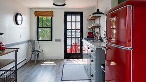A kitchen with a red refrigerator, a window with blinds, a chair, and a table with a blender.