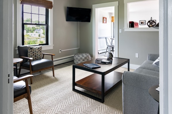 A modern living room with a sofa, armchair, coffee table, and a television mounted on the wall.