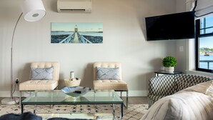 Un salón con dos sillones, una mesa de centro de vidrio, un televisor y un cuadro de un muelle.