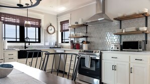 Una cocina moderna con armarios blancos, estufa de acero inoxidable, microondas y un reloj en la pared.