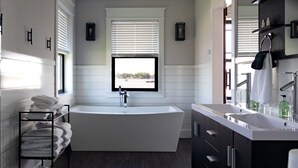 Un baño moderno con una bañera independiente, un espejo grande y un tocador con lavamanos.
