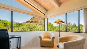 Una habitación con ventanas amplias, vista a una montaña, dos sillones, una mesita y una lámpara de pie.
