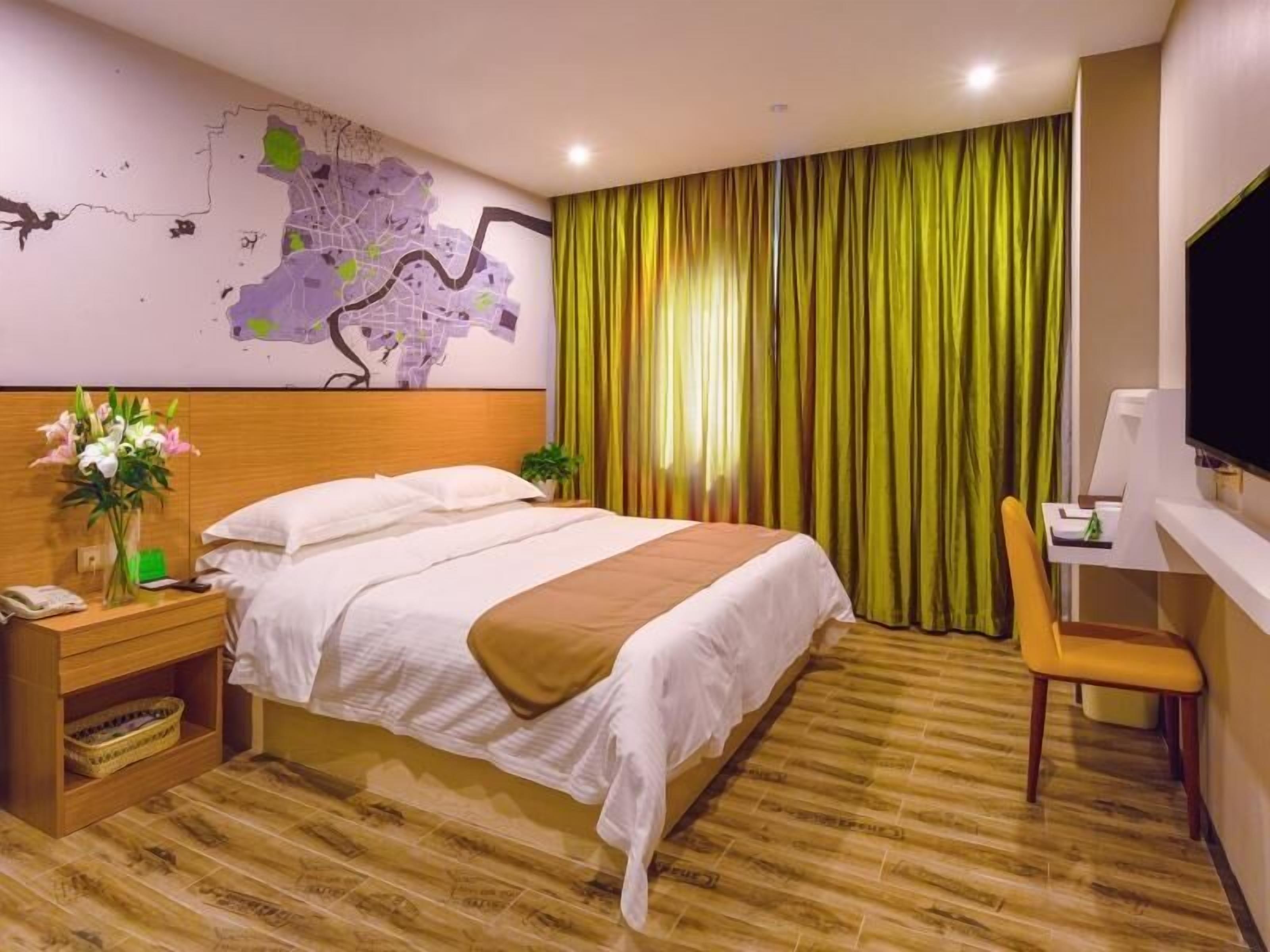 A hotel room with a bed, a desk, a chair, a map on the wall, and a curtain.