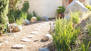 Una casa de piedra con puerta de madera, rodeada de un jardín con rocas y plantas.