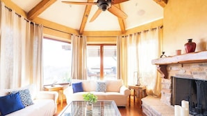 Una sala de estar acogedora con chimenea, ventilador de techo y un ventanal grande.