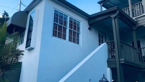 Un edificio de dos pisos con fachada blanca, un balcón en el nivel superior y una escalera que conduce a la entrada.