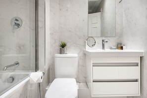 Un baño moderno con ducha de vidrio, inodoro, lavamanos con espejo y una pequeña planta en maceta.