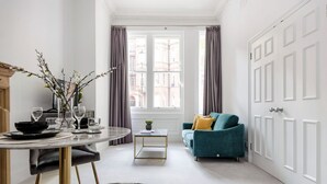 A modern living room with a dining area, a teal sofa, and a large window with curtains. - The Chelsea Studio next to Sloane Square (London)