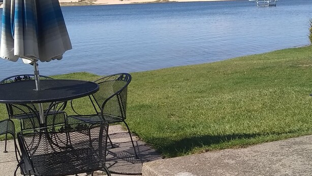 Ett bord och några stolar är uppställda på en betongterrass med utsikt över en sjö och sanddyner i bakgrunden.