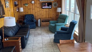 Ett vardagsrum med en svart lädersoffa, turkosa fåtöljer, ett träbord och en tv som är monterad på väggen.