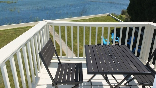 Une terrasse offrant une vue sur un plan d’eau, avec une table et deux chaises.