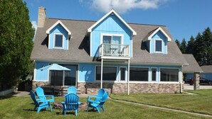 Une maison à deux étages, à l’extérieur bleu, avec un porche. On y trouve trois chaises Adirondack bleues sur la pelouse avant.