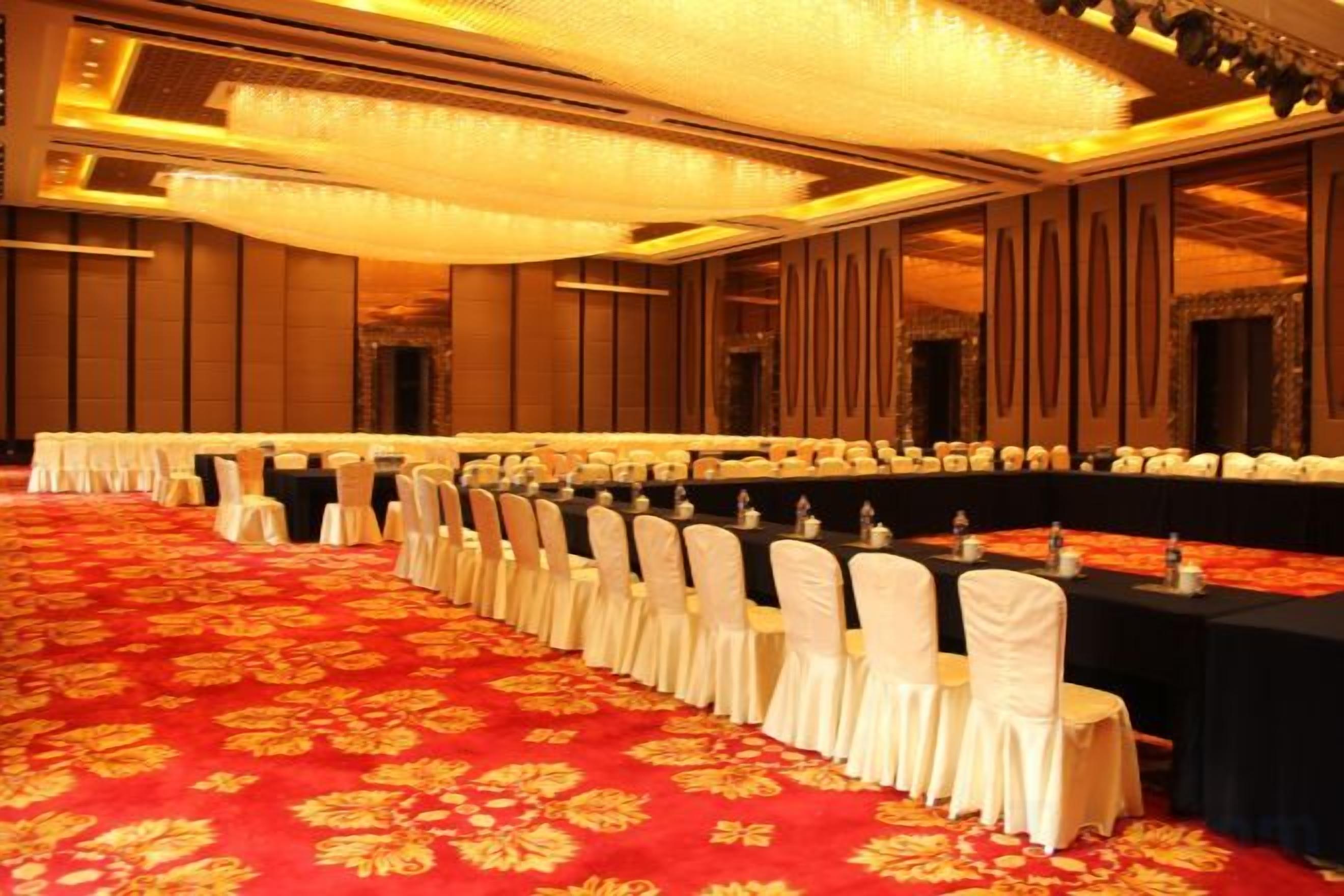 A banquet hall with rows of tables and chairs, a red carpet, and a chandelier.
