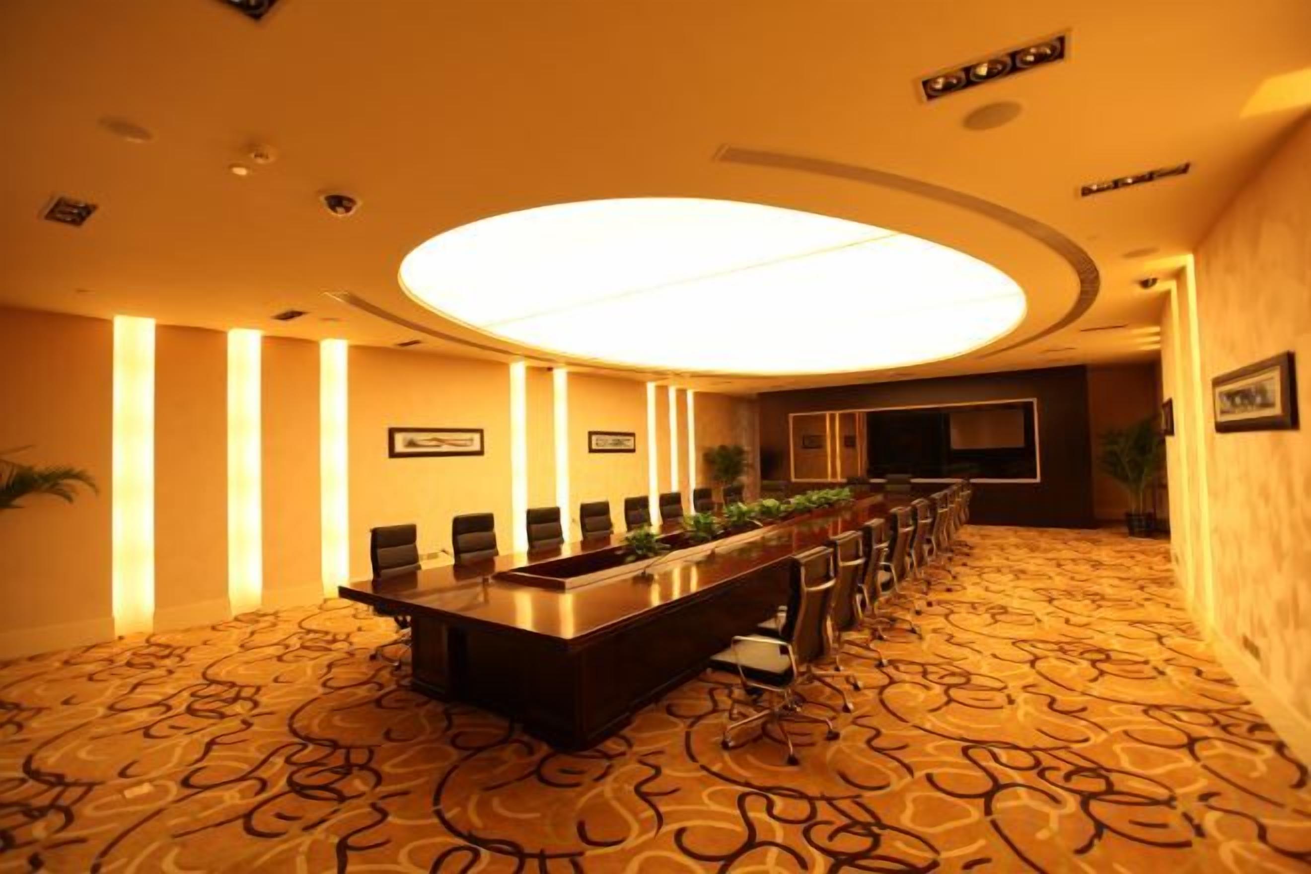 Un salón de conferencias con una mesa larga, sillas y una lámpara circular grande.