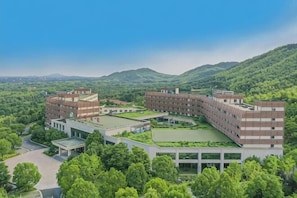A multi-story building with a central courtyard surrounded by greenery, set against a mountainous backdrop. - Jiangsu Yunhu International Conference Center (Yixing)