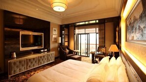 Habitación de hotel con una cama grande, televisión, zona de estar con una silla y mesa, y vistas al exterior.