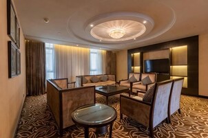 Habitación de hotel con un sofá, una mesa de centro, un televisor y una alfombra estampada.