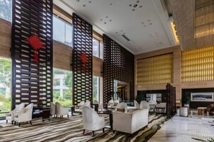 Un vestíbulo amplio con diseño moderno, que incluye un gran espacio de descanso, una chimenea y ventanas amplias con vistas al exterior.