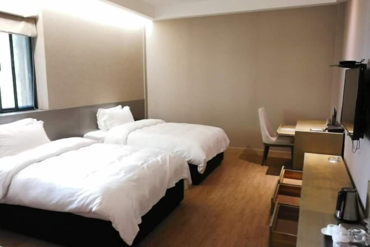 A hotel room with two beds, a desk, a chair, a TV, and a coffee maker.