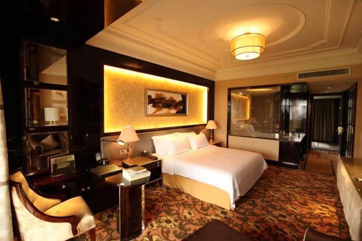 A hotel room with a large bed, two bedside tables, a desk with a chair, a mirror, and a patterned carpet.
