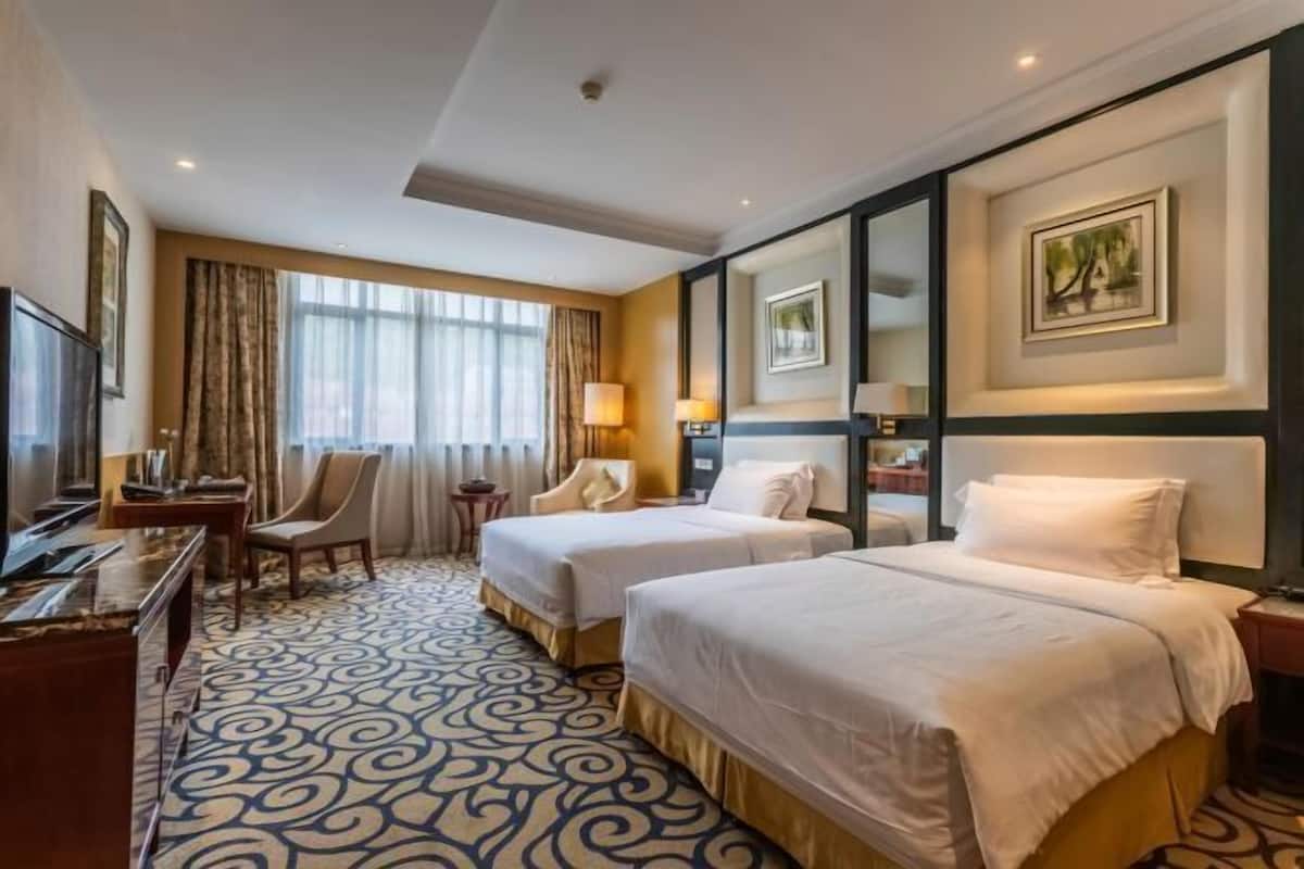 A hotel room with two beds, a desk, a chair, and a TV.