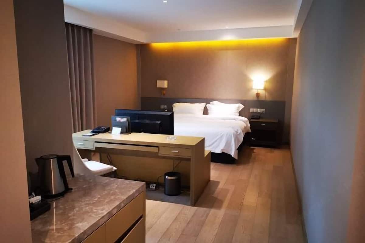 A hotel room with a bed, desk, and chair, a coffee maker, and a trash can.