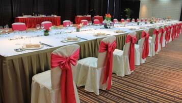 A banquet hall with long tables set for a formal event, each with a white tablecloth and red chair covers.