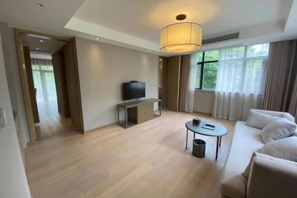 A modern hotel room with a sofa, a television, a small table, and a large window with curtains.