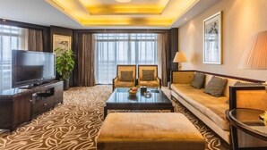 Habitación de hotel con televisor, sofá, sillón, mesa de centro y alfombra estampada.