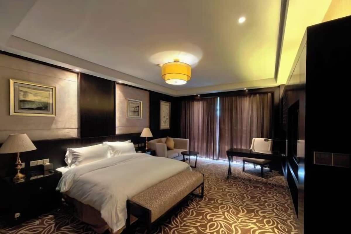 A hotel room with a large bed, bedside tables, a desk, a chair, a TV, and a patterned carpet.